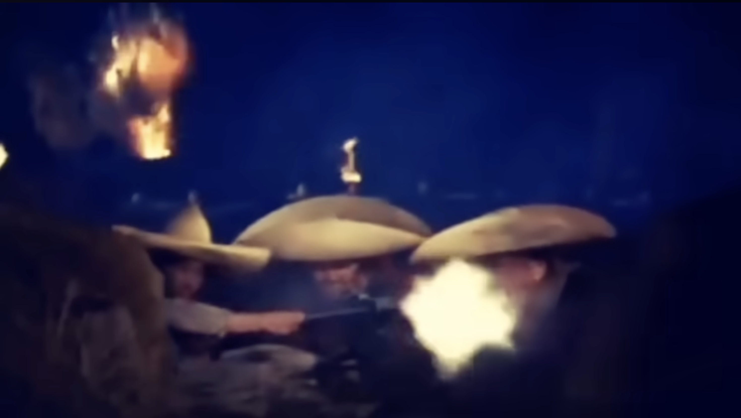 Still from La Cucaracha (1959) showing two soldiers in wide sombreros firing weapons at night, their faces lit by the muzzle flash against a dark sky.