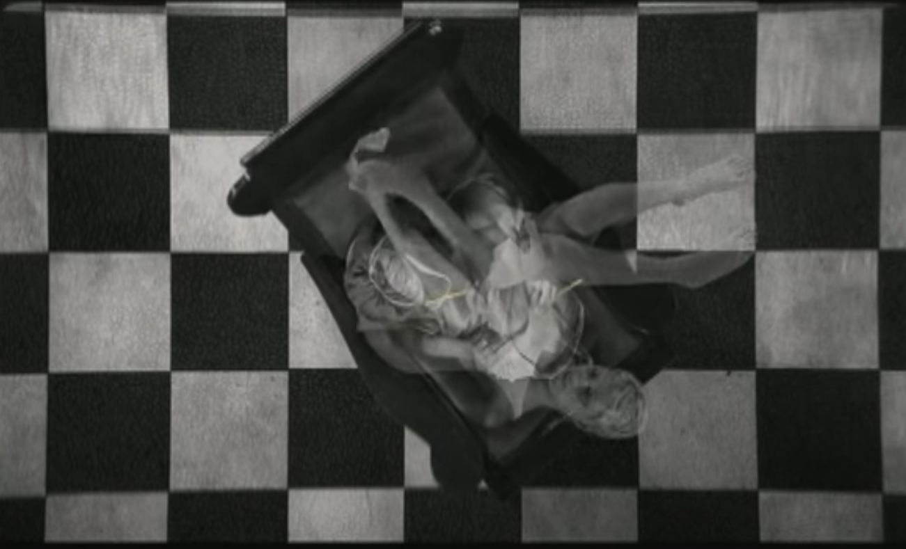 Carla superimposed upon herself during a transition as she writes a letter on a sofa