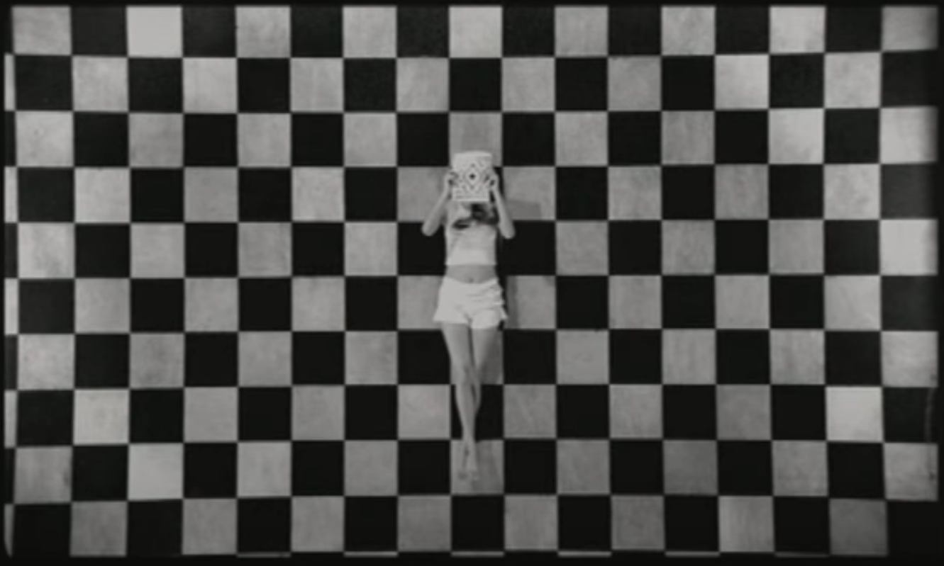 Carla lying flat on a checkered board floor while holding a magazine over her face
