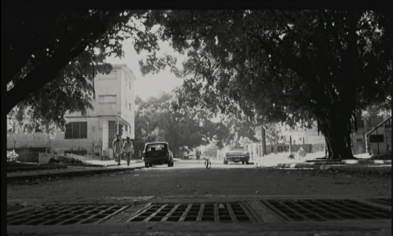 Black and white photo of the end of the car chase. César is biking away in the light while the tire remains stuck in the shadows.