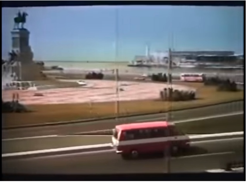 Opening scene with winding paved road and body of water in the background.