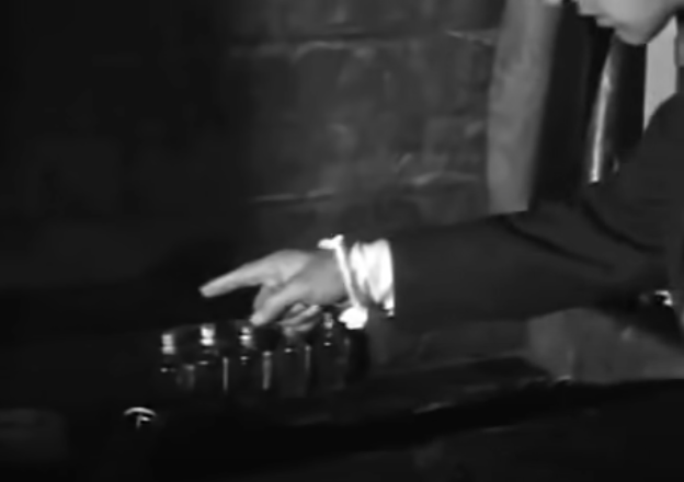 Macario counts how many vials he has left. His white shirt is seen poking out from under his dark jacket.