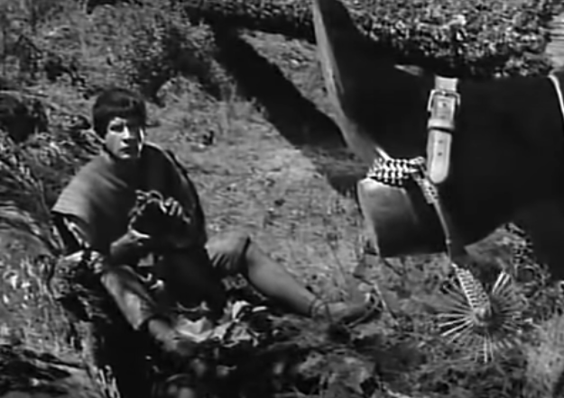 In the foreground, one of the boots that the Devil wears, in the background Macario looks up at him. Both are in focus.