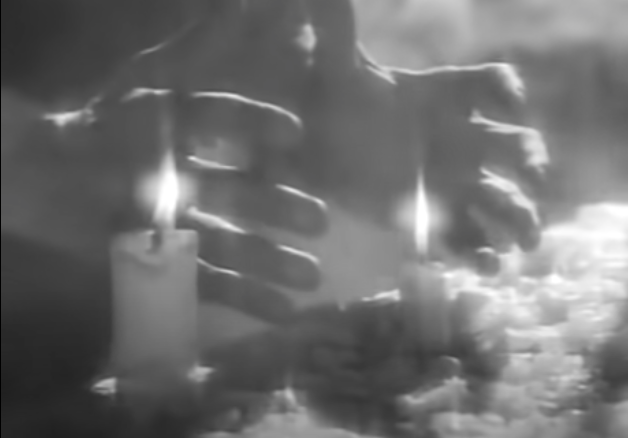 Death's hand are cupped around a diminishing candle.