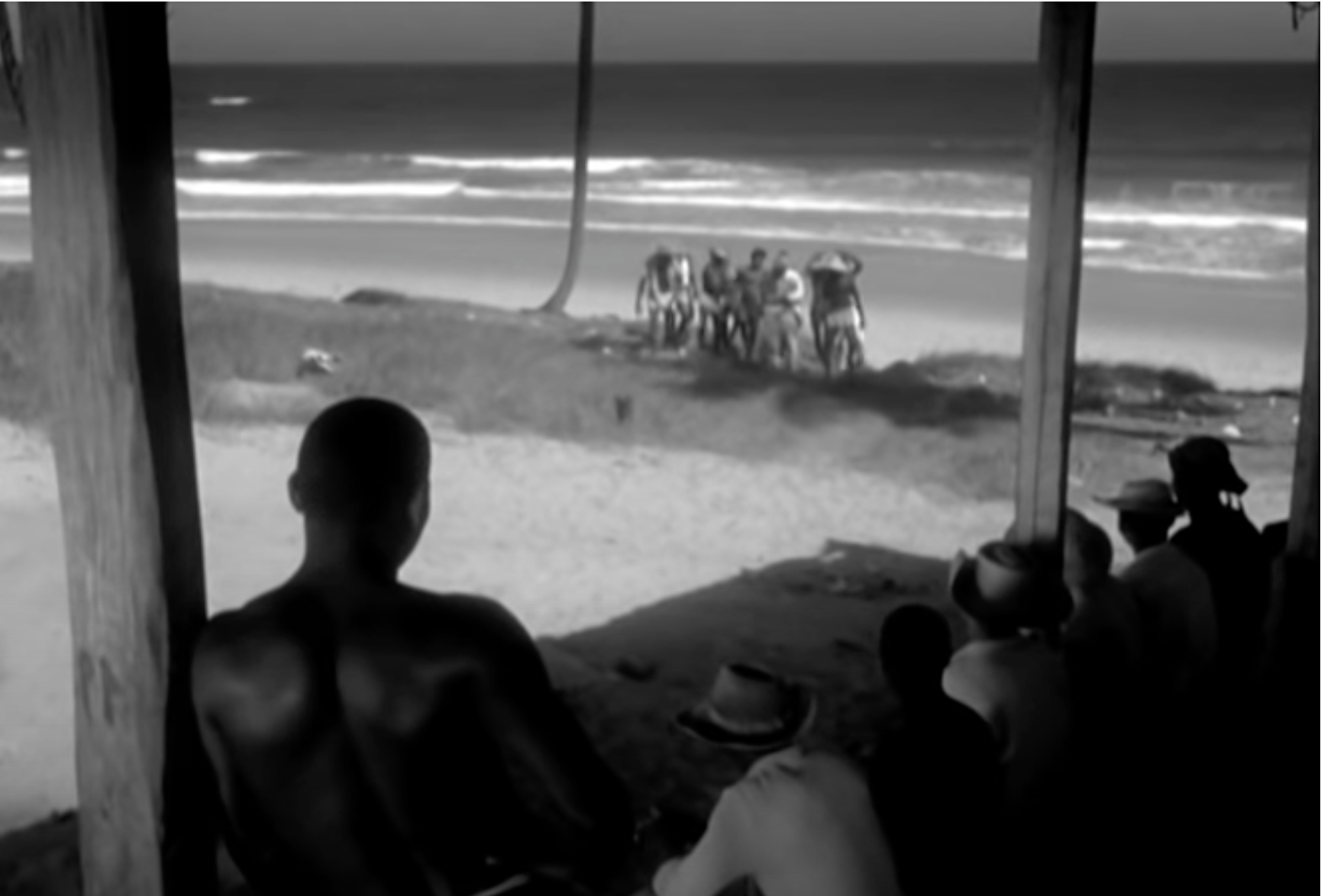 A shot from a hut showing men walking up from the beach.