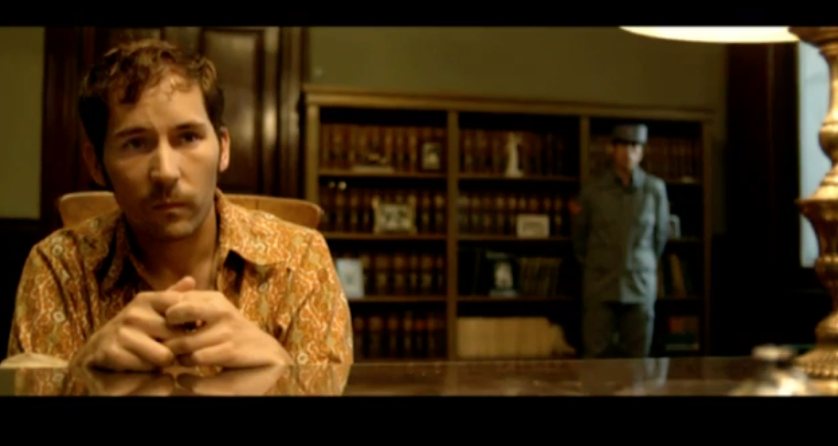 We see Isidoro wearing a 70s print orange and yellow floral blouse as he is interogated.