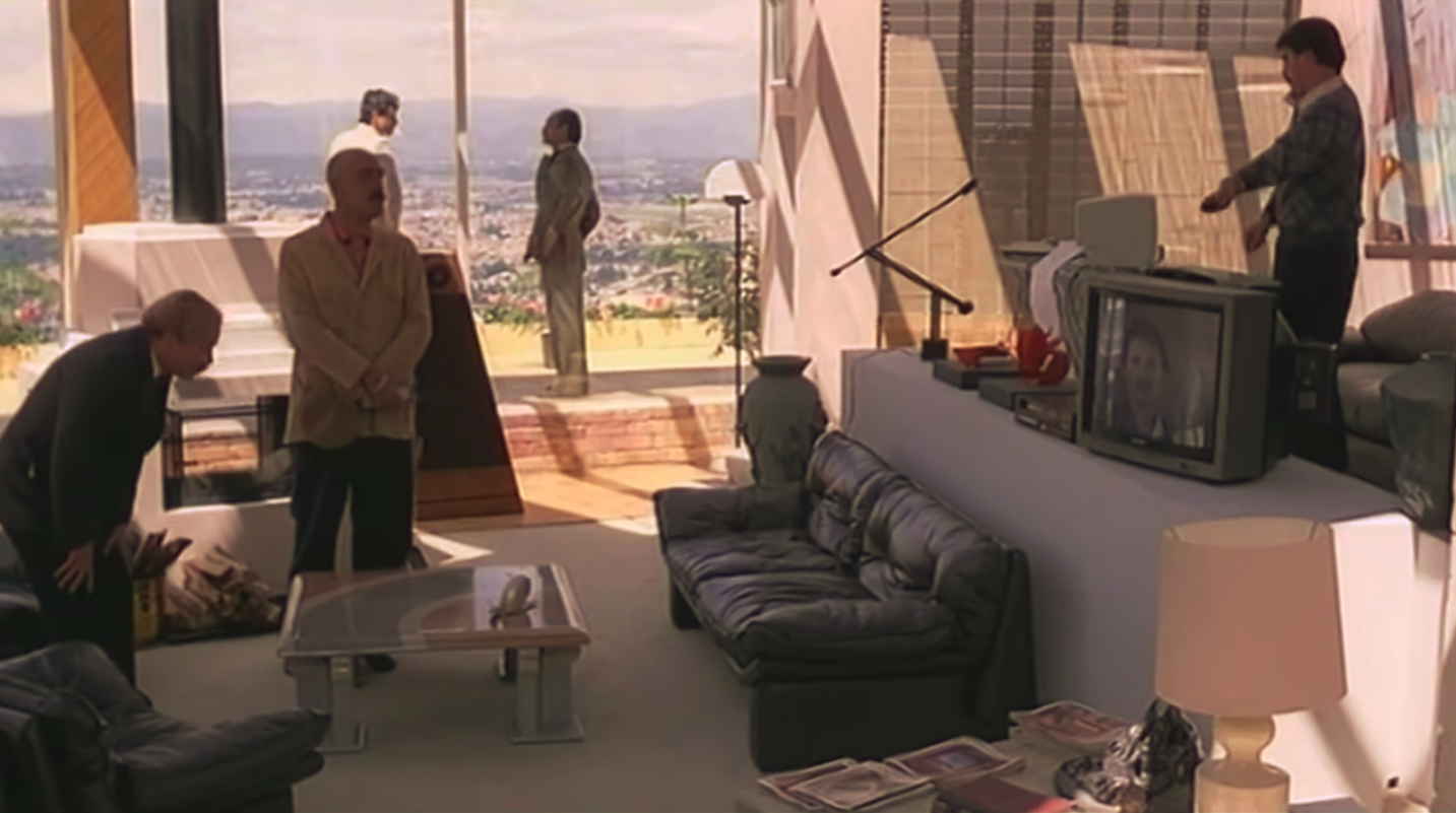 Dr. Holguín uses a remote to play a television message for his henchmen instead of talking to them directly.