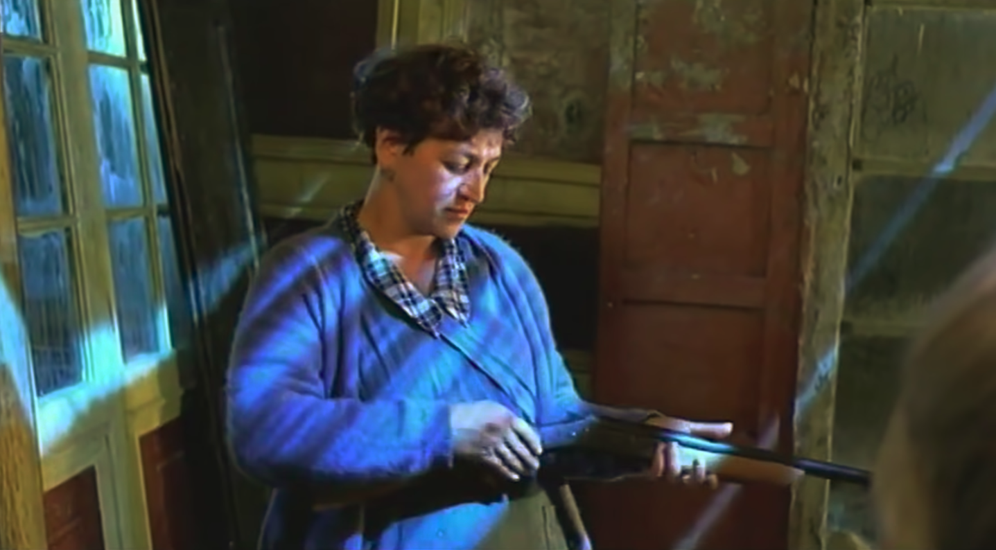 A woman holds a gun as blue moonlight blankets her from the windows above.