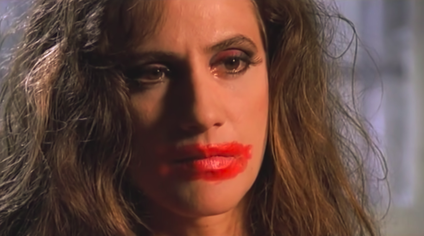 Gabriela can be seen with bright red lipstick covering her lips and cheeks in addition to heavy mascara/eyeshadow and her wig.