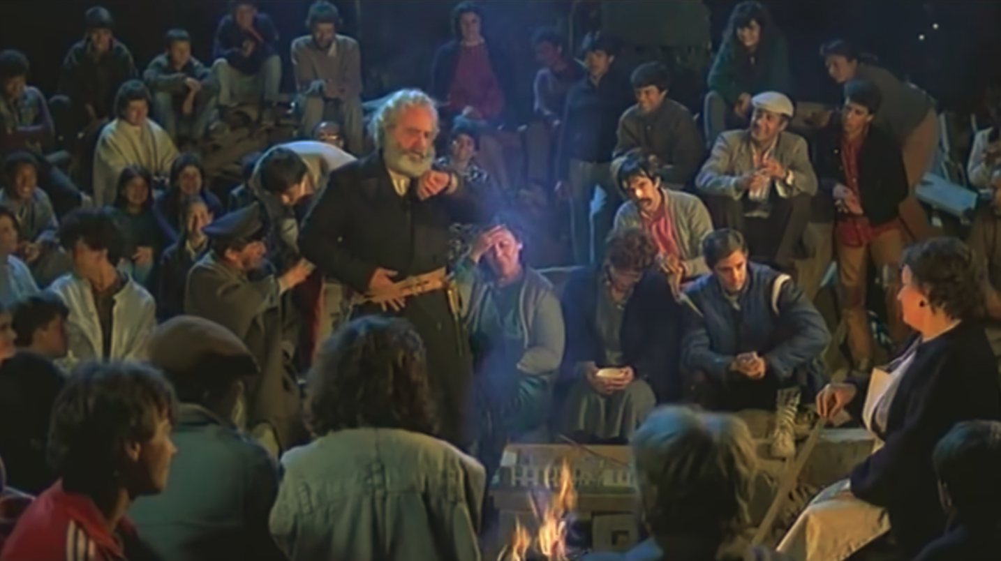 The squatters of the Casa Uribe can be seen gathered around a fire at night.