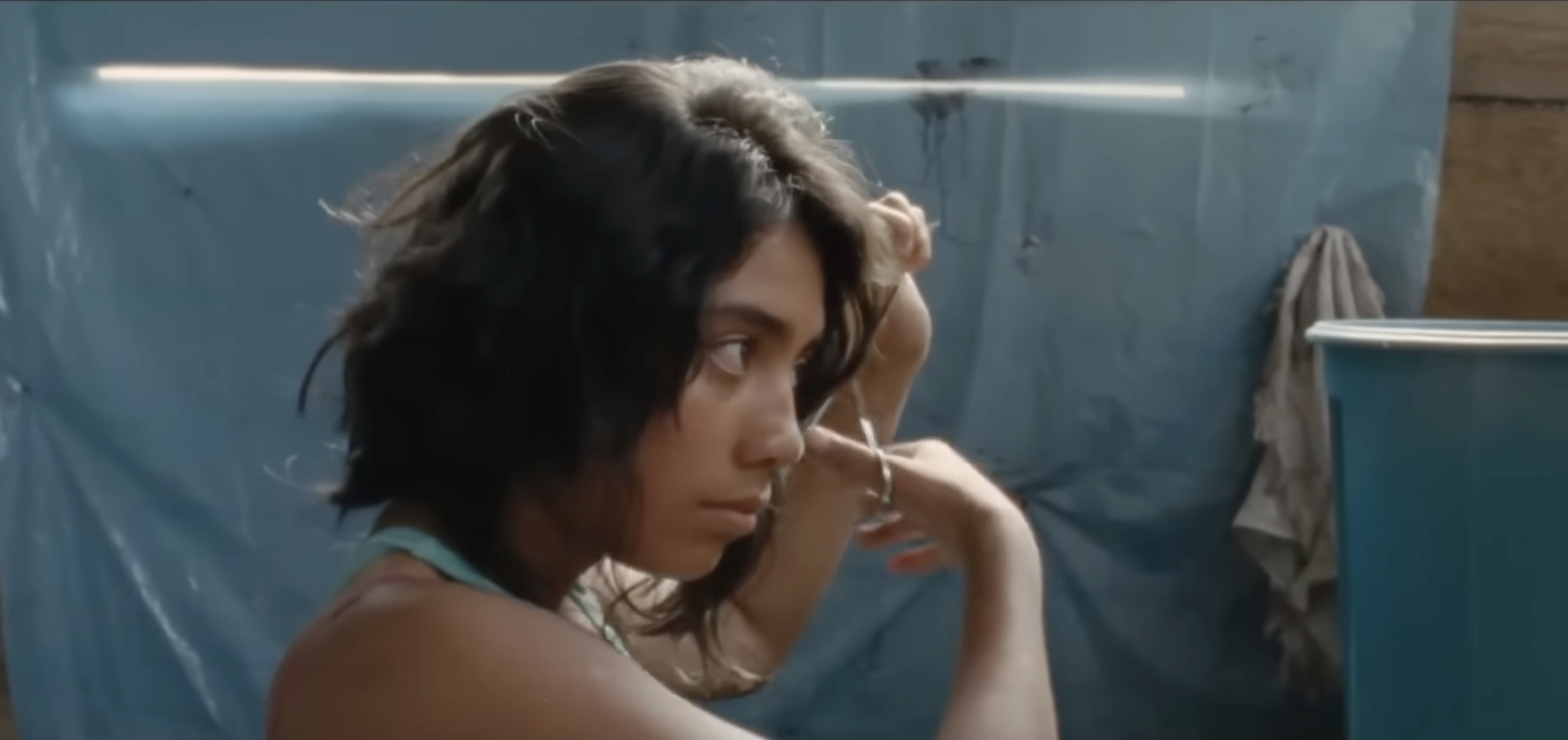 A teenage girl cuts her hair short in a small room with blue plastic tarp walls.