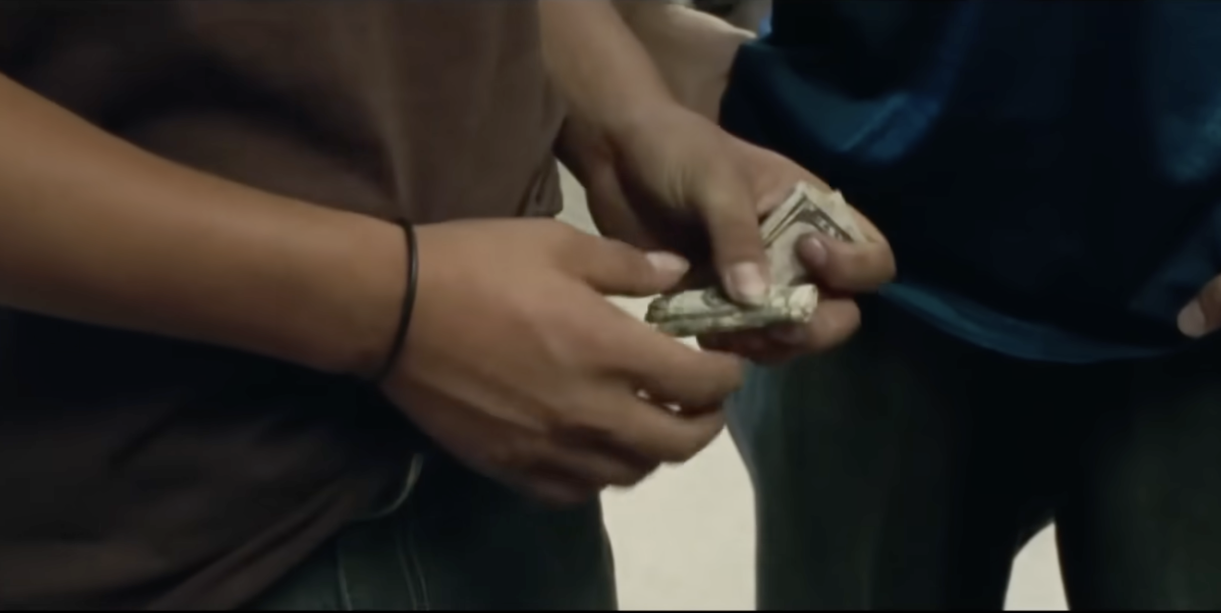Close-up of hands passing folded U.S. dollar bills from one person to another.