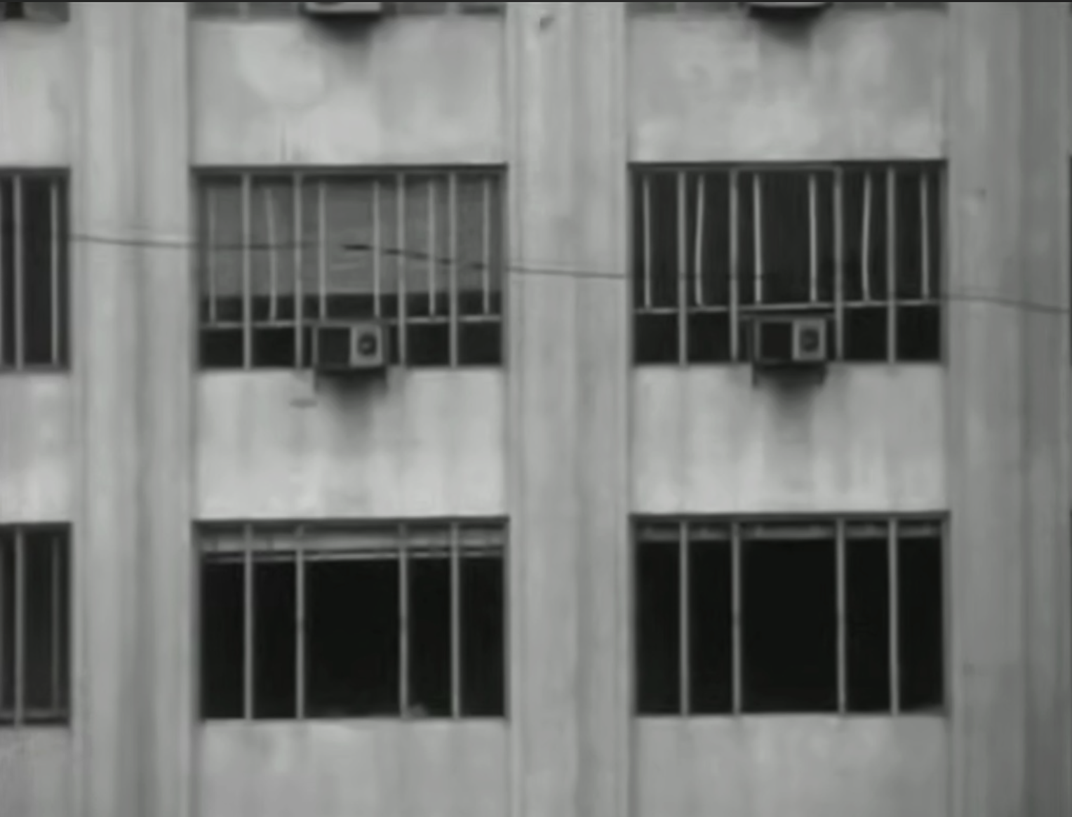 Shot on location in Buenos Aires, the camera captures the concrete exterior of a modern apartment building, defined by repeating rectangular window frames, AC units, and bare walls.