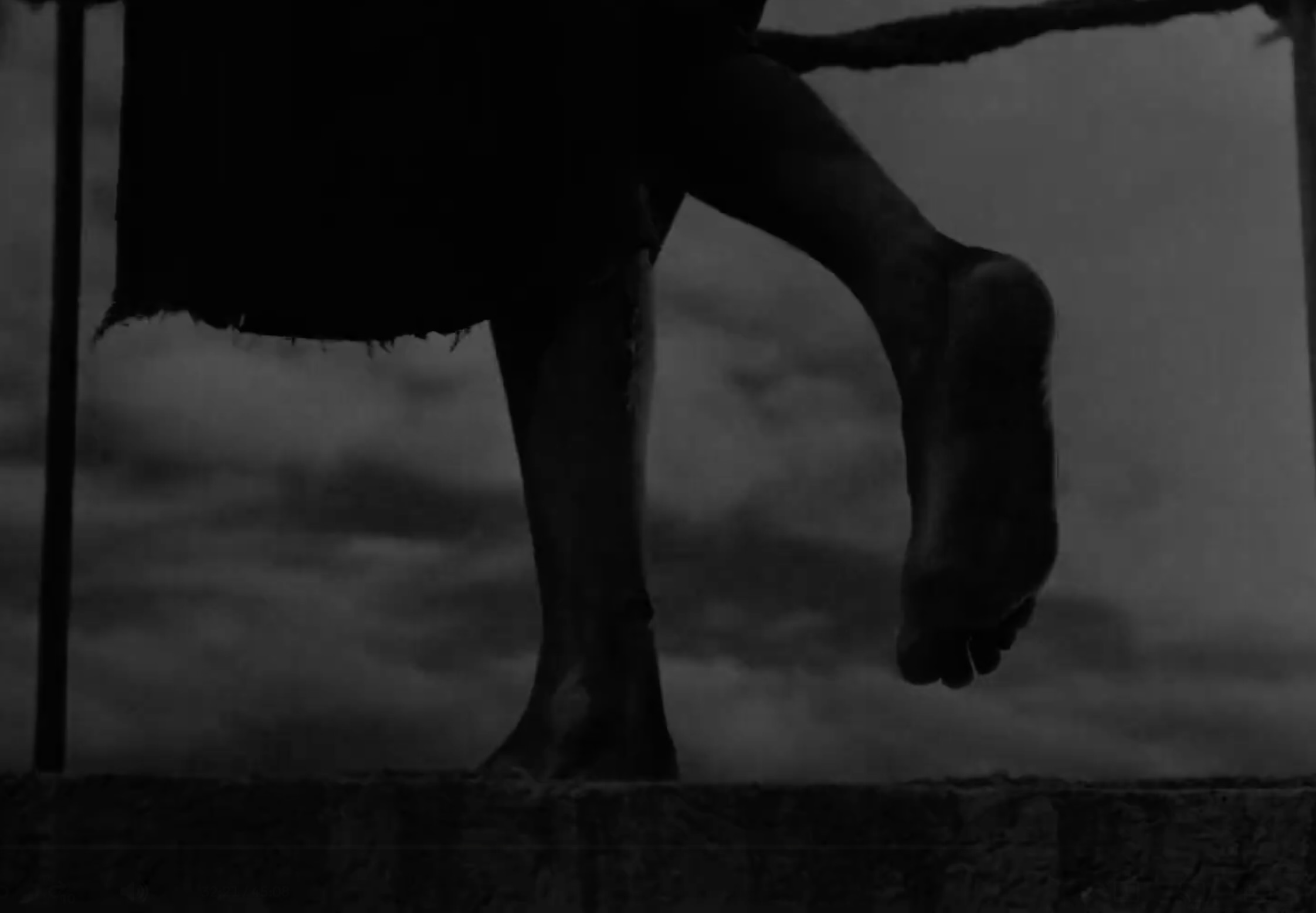 Simón forcing himself to stand on one foot as the light dims and scene transitions.