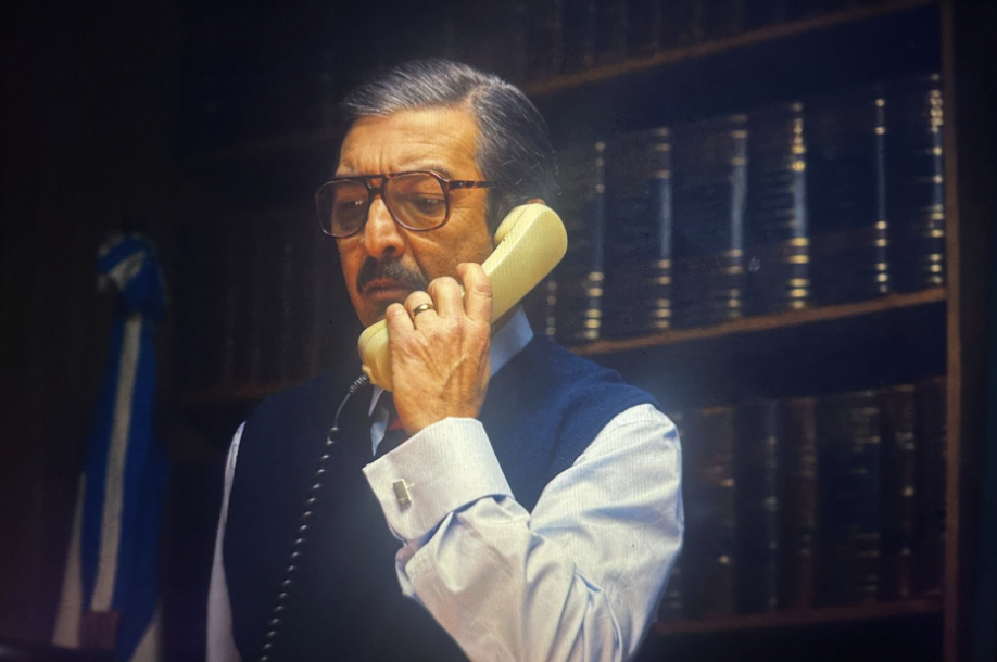 Julio Strassera addressing a case-related phone call with the Argentine flag looming behind him.
