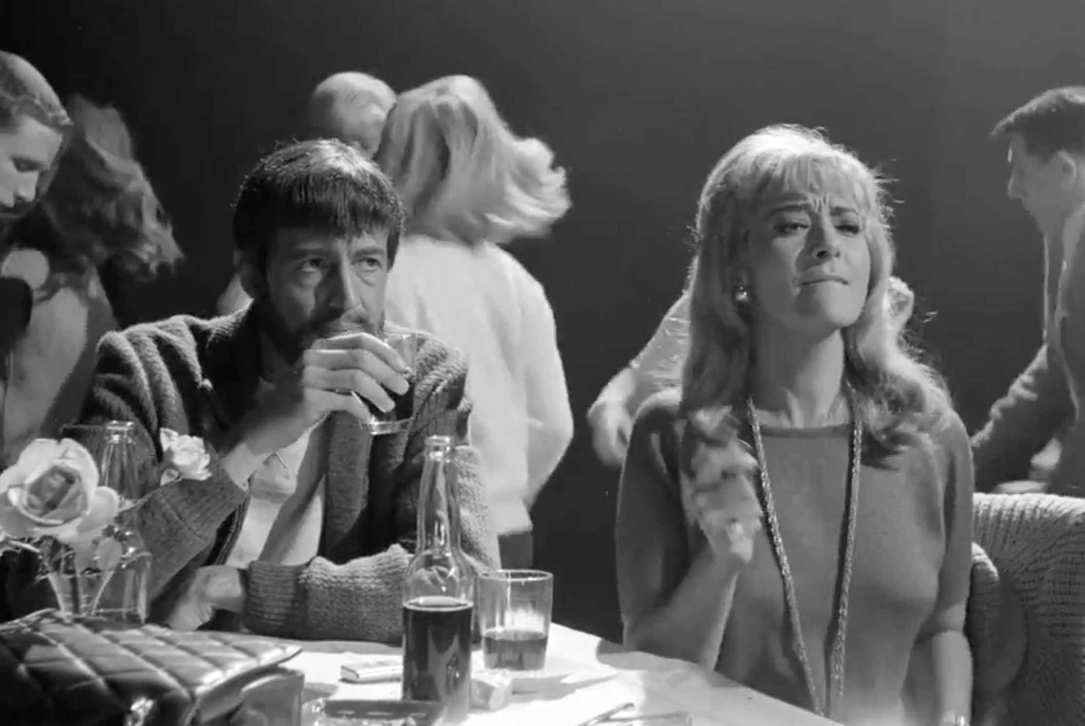 Simón and Satan in the bar wearing contemporary, formal clothing in the modern-day nightclub.