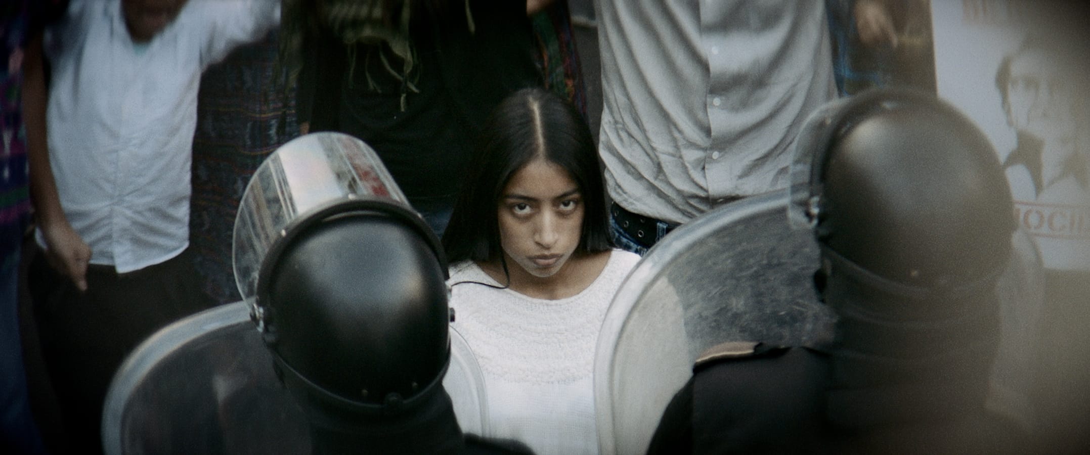 Alma en la multitud protestando la genocida instituida por el General, mirando fijamente a la familia en su vestido largo y blanco. 