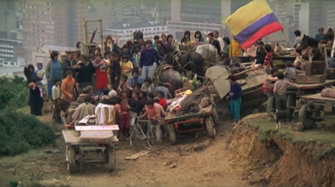 Dozens of inhabitants gather atop a hill overlooking Bogotá while proudly displaying the stolen pieces of the house in addition to the Colombian flag.