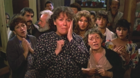 The inhabitants pray together in front of the camera after discovering a miracle hidden in the walls of the Casa Uribe. In the background some skeptics chat amongst themselves.