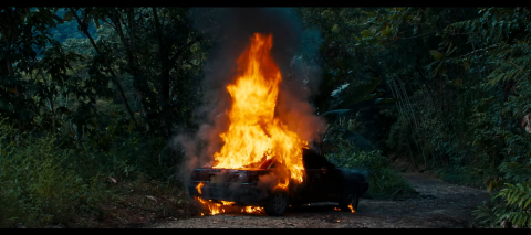 A car on fire in a forest.