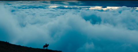 Man on horseback backdropped against clouds.