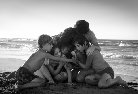 A black and white picture of a family hugging their housekeeper on the beach.